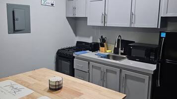 A kitchen with white cabinets, a stove, a sink, and a refrigerator. There are signs on the wall and a table with a roll of paper towels.