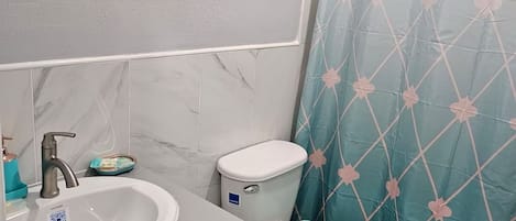 Un baño con un lavamanos blanco, un inodoro y una cortina de ducha con diseño geométrico.