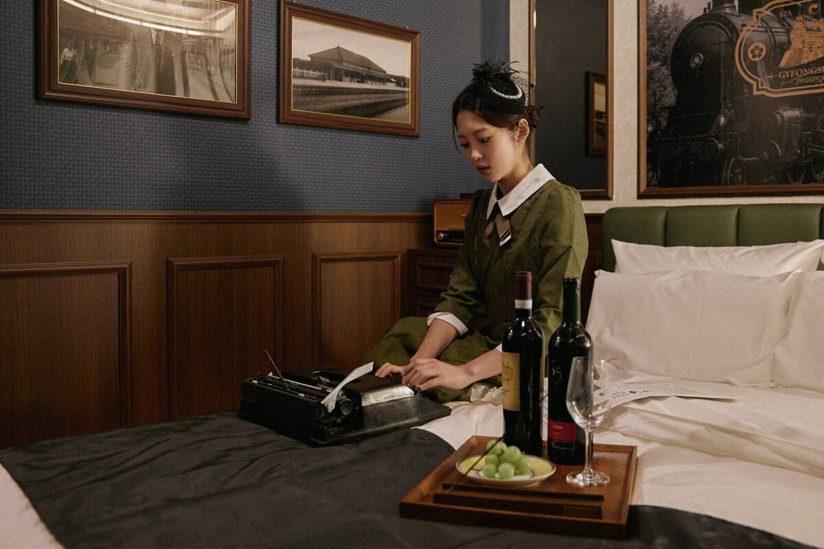 Una habitación con una cama, un piano, una bandeja con botellas de vino y uvas, y cuadros en la pared.