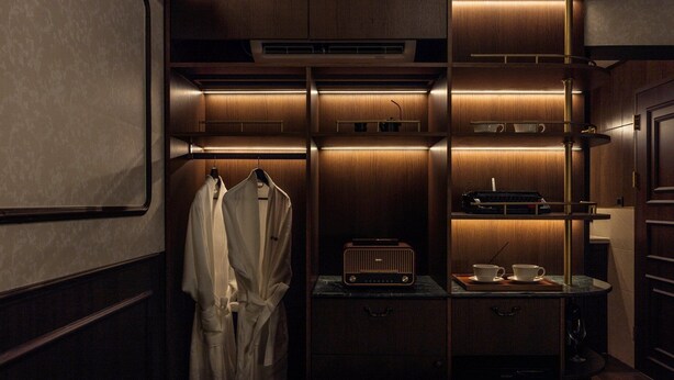 Ein kompakter, gut beleuchteter begehbarer Kleiderschrank mit Holzschränken, einem Kleiderbügel und einem kleinen Tischchen mit Radio und Tassen.