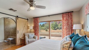 Een slaapkamer met een groot bed, een stoel, een kleine tafel en uitzicht op het groen door een schuifdeur.