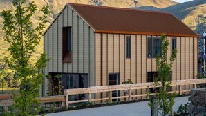 A modern building with a sloped roof, large windows, and a wooden fence in front. - The Pisa (Cardrona)