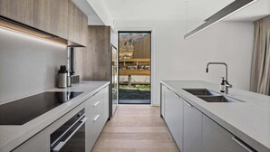 A modern kitchen with a central island, stainless steel appliances, and a view of a mountainous landscape through an open door. - The Pisa (Cardrona)