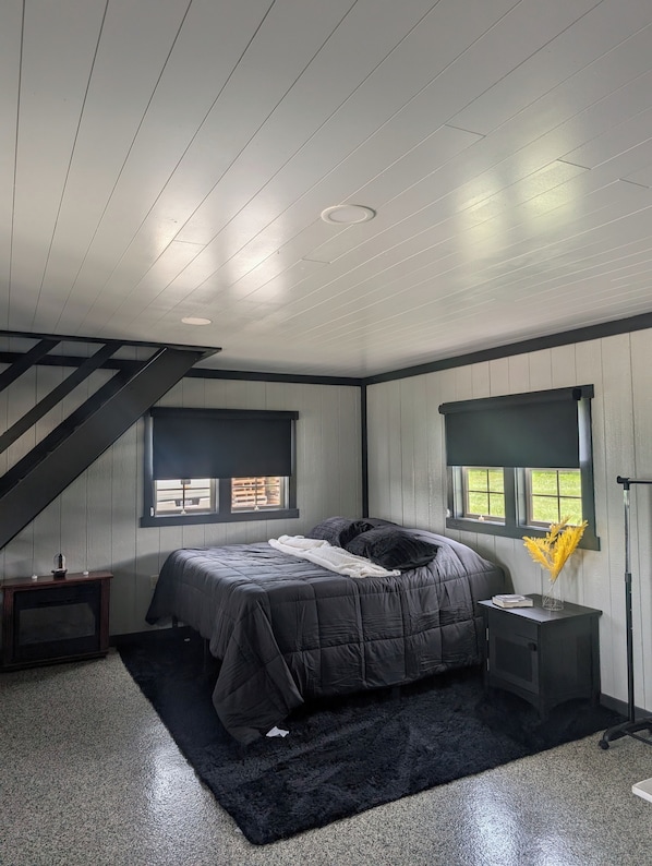 Ein Schlafzimmer mit einem Bett, einem Nachttisch, einer Lampe, einem Fenster und einer Treppe.