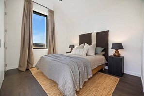 Ein Schlafzimmer mit einem Bett, zwei Nachttischen, einem Fenster mit Vorhängen und Blick ins Freie.