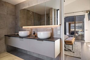 Ein modernes Badezimmer mit zwei großen Waschbecken, einem großen Spiegel und Blick auf einen Essbereich durch eine Glastür.