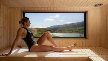 Una persona sentada en un tapete dentro de una habitación de madera con un ventanal grande que da a un paisaje.