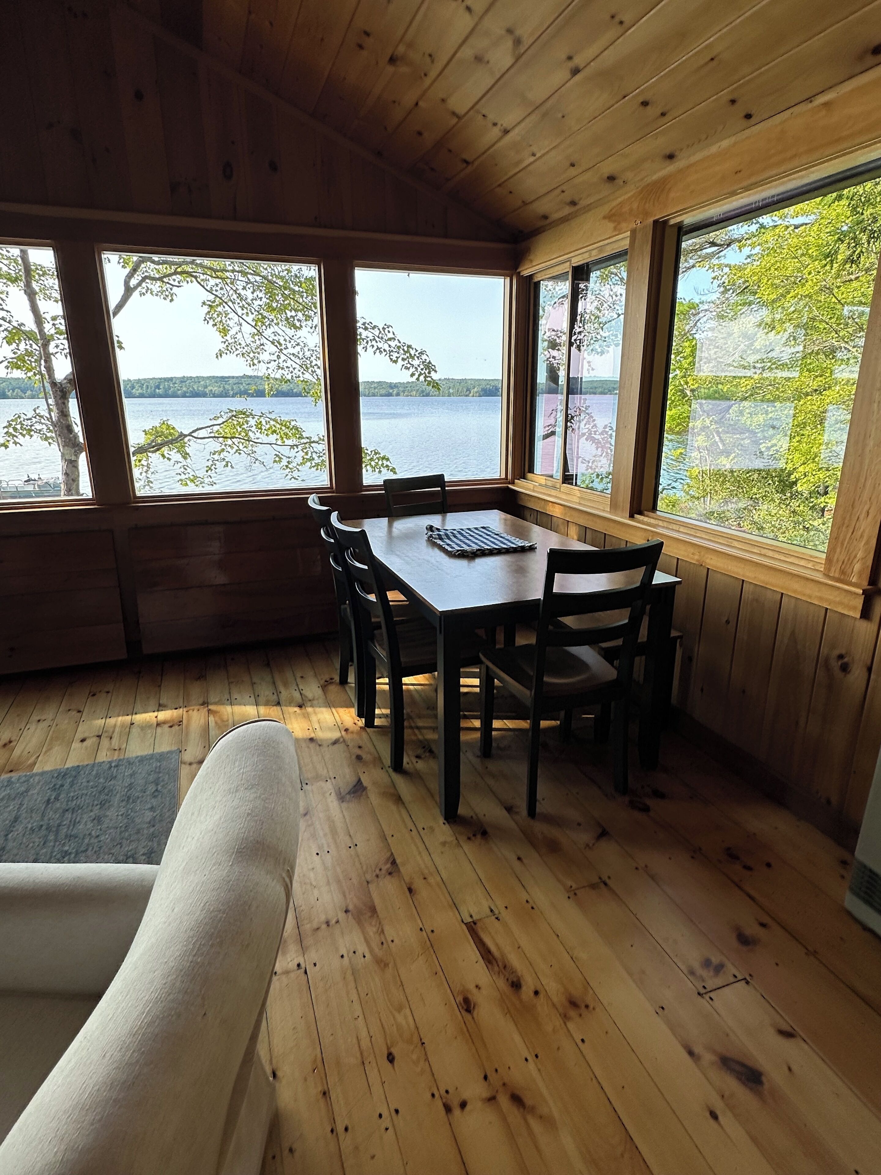 Une cabane en bois avec une table et des chaises, de grandes fenêtres donnant sur un lac et un intérieur chaleureux.