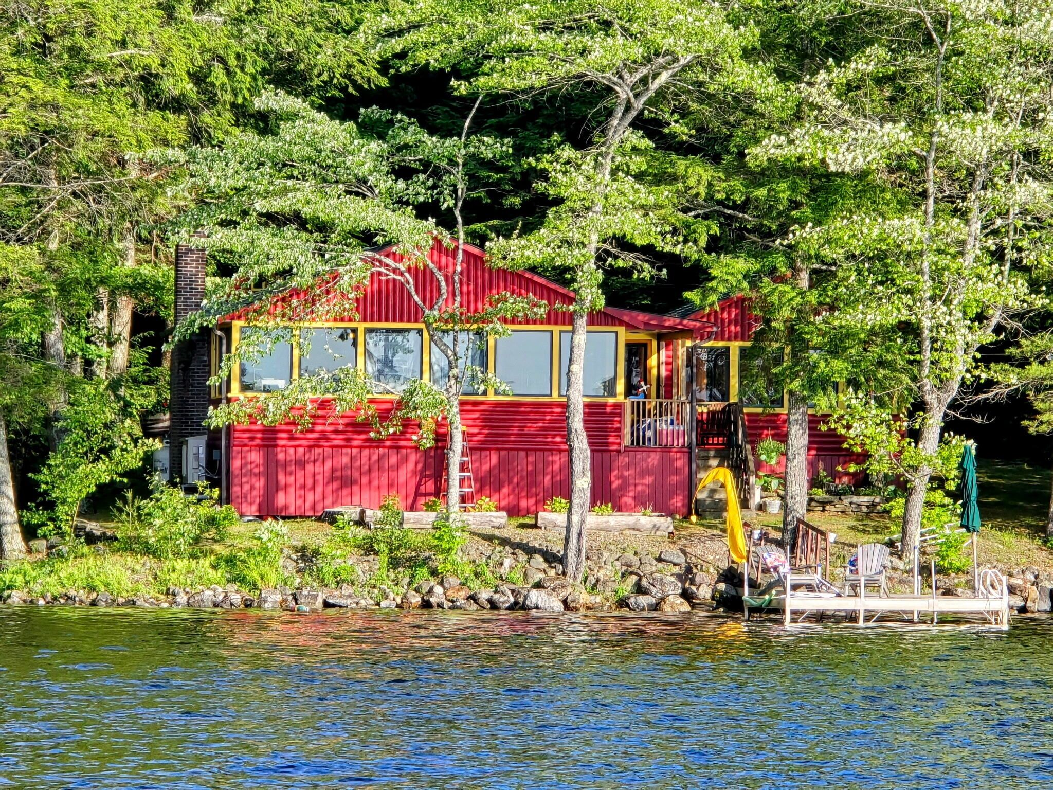 Une cabane rouge avec un quai, entourée d’arbres et bordant un lac.