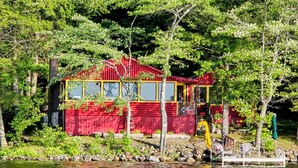A red cabin with a dock, surrounded by trees and a lake.