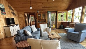 A cozy cabin interior with wooden walls, a television, a sofa, a chair, and a table.