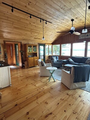 A wooden cabin interior with a dining area, a sofa, and a kitchen. - Cozy lakefront cabin on Damariscotta Lake, relax & enjoy summer as it should be. (Jefferson)