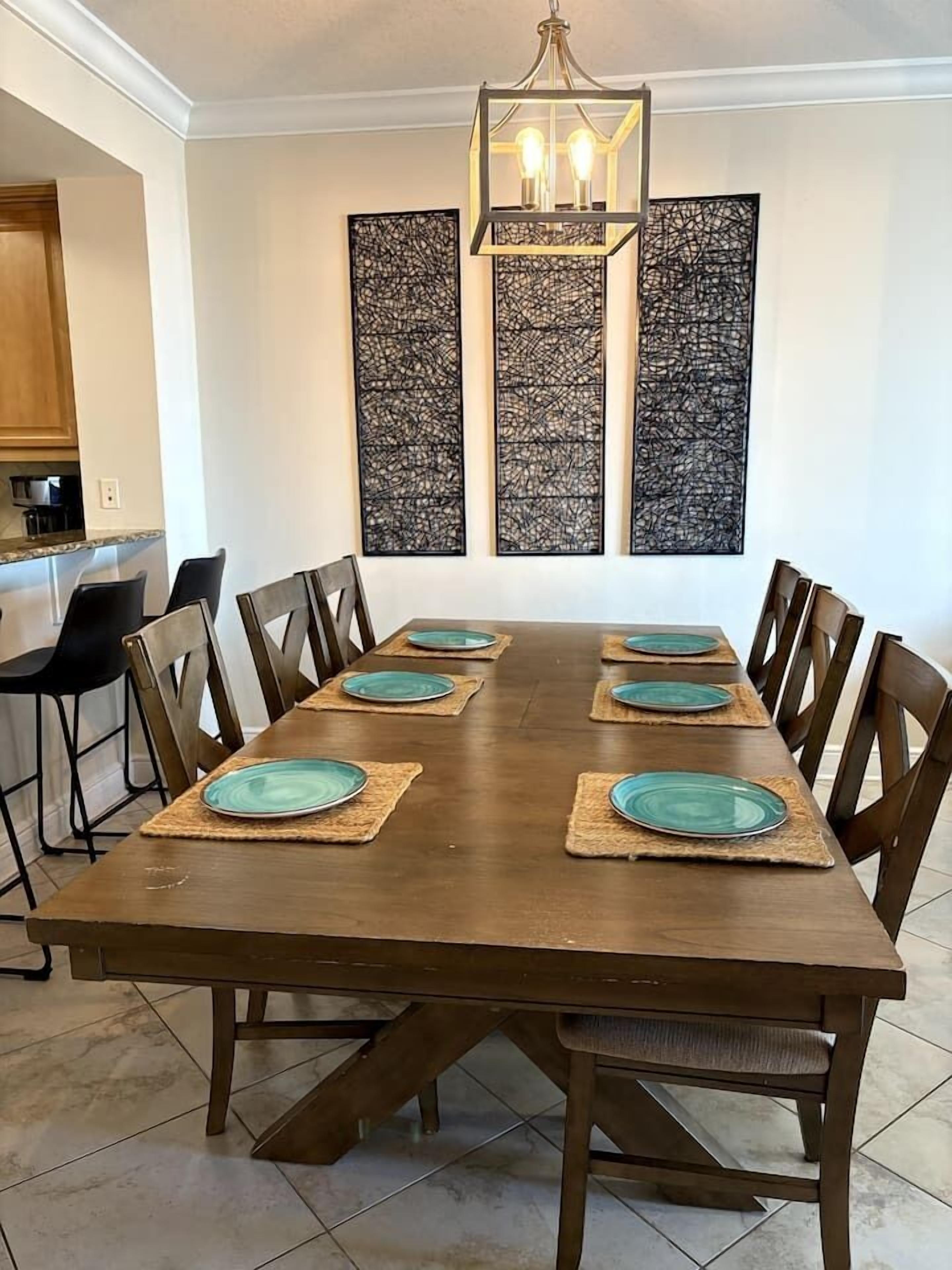 A dining room with a long wooden table, six chairs, and three abstract wall art pieces.