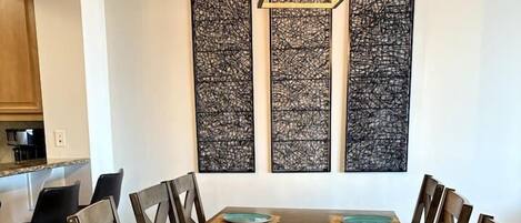 A dining room with a long wooden table, six chairs, and three abstract wall art pieces.