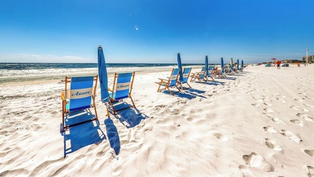 A beach with rows of blue beach chairs and umbrellas, a clear sky, and the ocean in the background. - 3BR ~ Beachfront ~ Huge Balcony ~ 2 Pools ~ Luxury (Fort Walton Beach)
