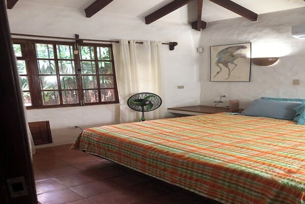 Une chambre à coucher comprenant un lit, une fenêtre, un ventilateur et une œuvre d’art accrochée au mur.