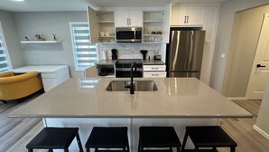 A modern kitchen with white cabinets, a stainless steel refrigerator, a built-in microwave, and a large island with a sink. There are four black stools around the island. - ✨your home away from home✨Modern
Comfort in a spacious 3-Bedroom Townhome (Airdrie)
