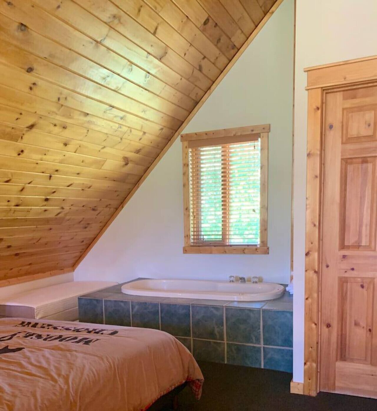 A bedroom with a sloped wooden ceiling, a built-in bathtub, and a wooden door.