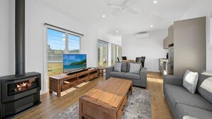Een moderne woonkamer met een houtkachel, een flatscreen televisie, een grijze bank en een houten salontafel.