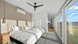 Een moderne slaapkamer met een groot bed, een plafondventilator en uitzicht op de omgeving door grote ramen.