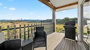 Een overdekt terras buiten met rieten stoelen en een barbecue, met uitzicht op een prachtig landschap.