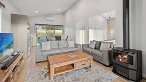Ein modernes Wohnzimmer mit Kamin, grauen Sofas, einem Holztisch und einem großen Fenster mit Blick ins Freie.