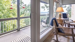 A balcony with a view of greenery and a body of water. There is a wicker chair with cushions and a table with a lamp. - Cliffside Escape – Cozy 2BR/2BA Condo with Scenic Views (Fairfield Bay)