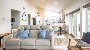 A modern living room with a beige sofa, a dining area, and a kitchen in the background. - Cliffside Escape – Cozy 2BR/2BA Condo with Scenic Views (Fairfield Bay)