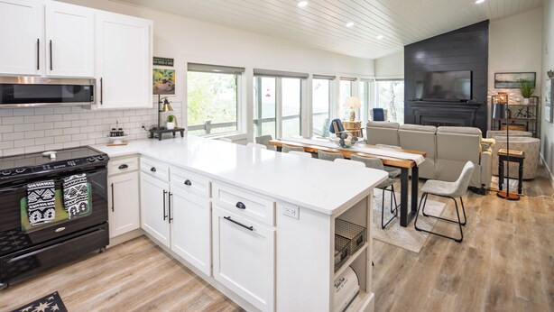 A modern kitchen with white cabinetry, a black stove, and a dining area with a table and chairs. - Cliffside Escape – Cozy 2BR/2BA Condo with Scenic Views (Fairfield Bay)