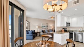 A modern kitchen with white cabinets, a microwave, and a dishwasher. There is a dining area with a wooden table and chairs, and a bowl of decorative items on the table. - Beachfront Penthouse 1BR @ Phoenix X • Sleeps 6 • Stunning Views & Next to Flora-Bama (Orange Beach)