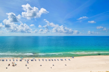 A beach with clear blue water, white sand, and a few umbrellas.
