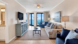 A living room with a sofa, a coffee table, a TV, and a balcony with a view. - Beachfront Penthouse 1BR @ Phoenix X • Sleeps 6 • Stunning Views & Next to Flora-Bama (Orange Beach)