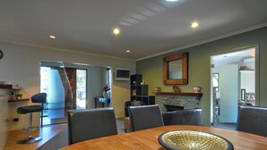A dining area with a round table, chairs, a decorative bowl, a stone fireplace, and a television. - Cute As, by the lake, bike tracks walking distance to shops & retail !! (Queenstown)