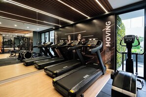 Ein modernes Fitnessstudio mit Laufbändern, einem an der Wand befestigten Hometrainer und einem Spiegel, der den Raum widerspiegelt.