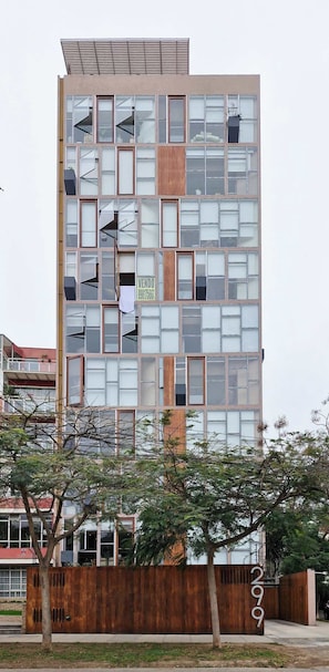 Um edifício moderno de vários andares, com uma combinação de painéis de vidro e madeira, e uma placa visível 'VENIDO'.