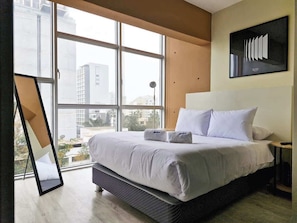 Quarto de hotel moderno com uma cama grande, vista para a cidade e uma obra de arte emoldurada na parede.
