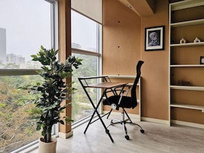 Ein moderner Arbeitsraum mit großem Fenster, Schreibtisch, Stuhl, Bücherregal und einem Blumentopf.