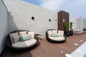 Zwei runde Korbssofas mit Kissen, ein Holzdeck, eine geflieste Wand und ein Blumentopf.