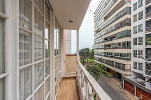 Een balkon met grote ramen, een houten vloer en uitzicht op omliggende gebouwen.