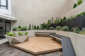 Un patio interior con suelo de madera, paredes de hormigón y diversas plantas.