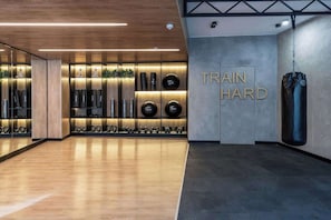 Un gimnasio con piso de madera, un saco de boxeo y una pared con la inscripción 'TRAIN HARD'.