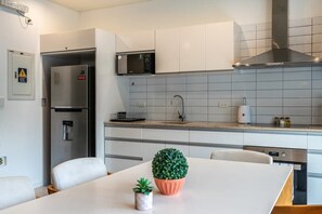 A modern kitchen with white cabinets, a stainless steel refrigerator, a microwave, and a stove. There is a small potted plant on the counter.