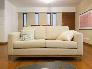 Ein beiges Sofa mit zwei Kissen, ein Holzboden und ein gerahmtes abstraktes Gemälde an der Wand.