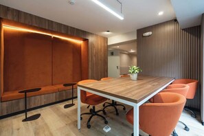 Une salle de conférence avec une table en bois, des chaises orange, un banc et une plante en pot.
