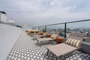 Une terrasse sur le toit, dotée de chaises longues et d’un sol à motifs, offrant une vue sur la ville.