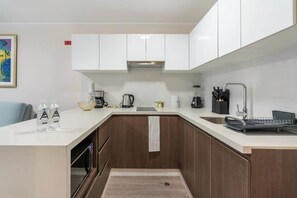 A modern kitchen with white cabinets, a stainless steel range hood, and a built-in oven.