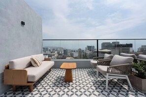 A rooftop terrace with a sofa, chairs, a small table, and a patterned floor.