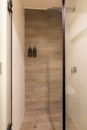 Ein Duschbereich mit Holzwand, Glastür und zwei Shampoo-Flaschen.