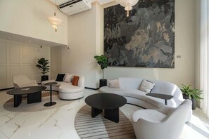 A modern living room with a white sofa, two black coffee tables, and a large abstract painting on the wall.
