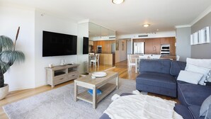 A modern living room with a flat-screen TV, a wooden coffee table, a blue sofa, and a large mirror.
